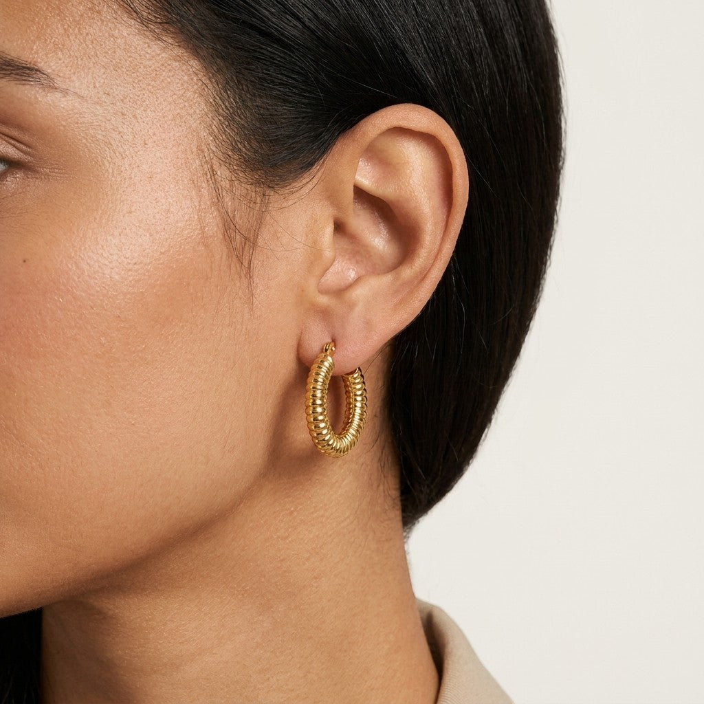 Aramat Jewels gold-tone stainless steel hoop earrings with a ribbed stripe pattern, 22x4mm, worn by a model.