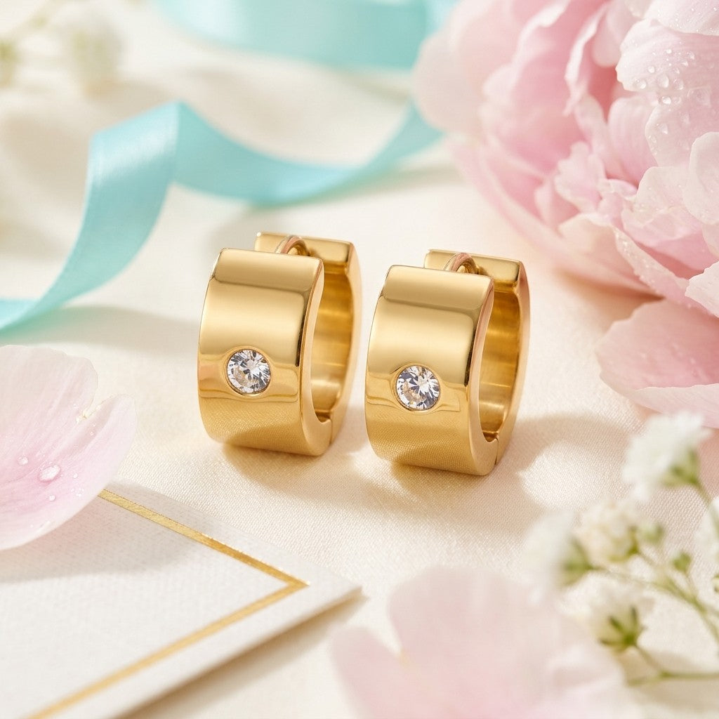 Aramat Jewels gold-colored wide stainless steel huggie hoop earrings with a single clear cubic zirconia stone.