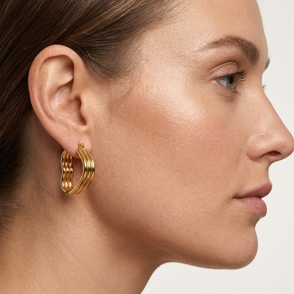 Aramat Jewels gold-tone triple heart hoop earrings with a hinged closure, worn by a model.