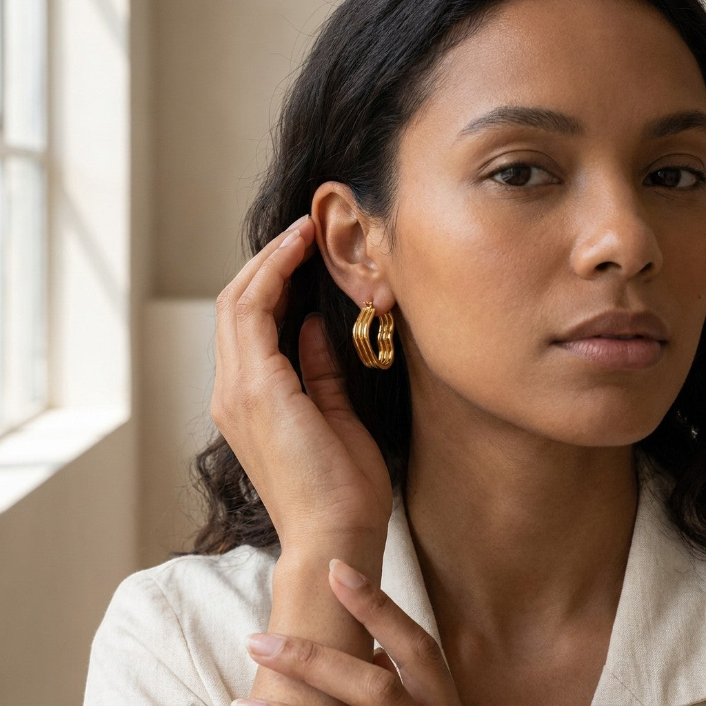 Aramat Jewels gold-tone triple heart hoop earrings worn by a woman with dark wavy hair and tan skin.