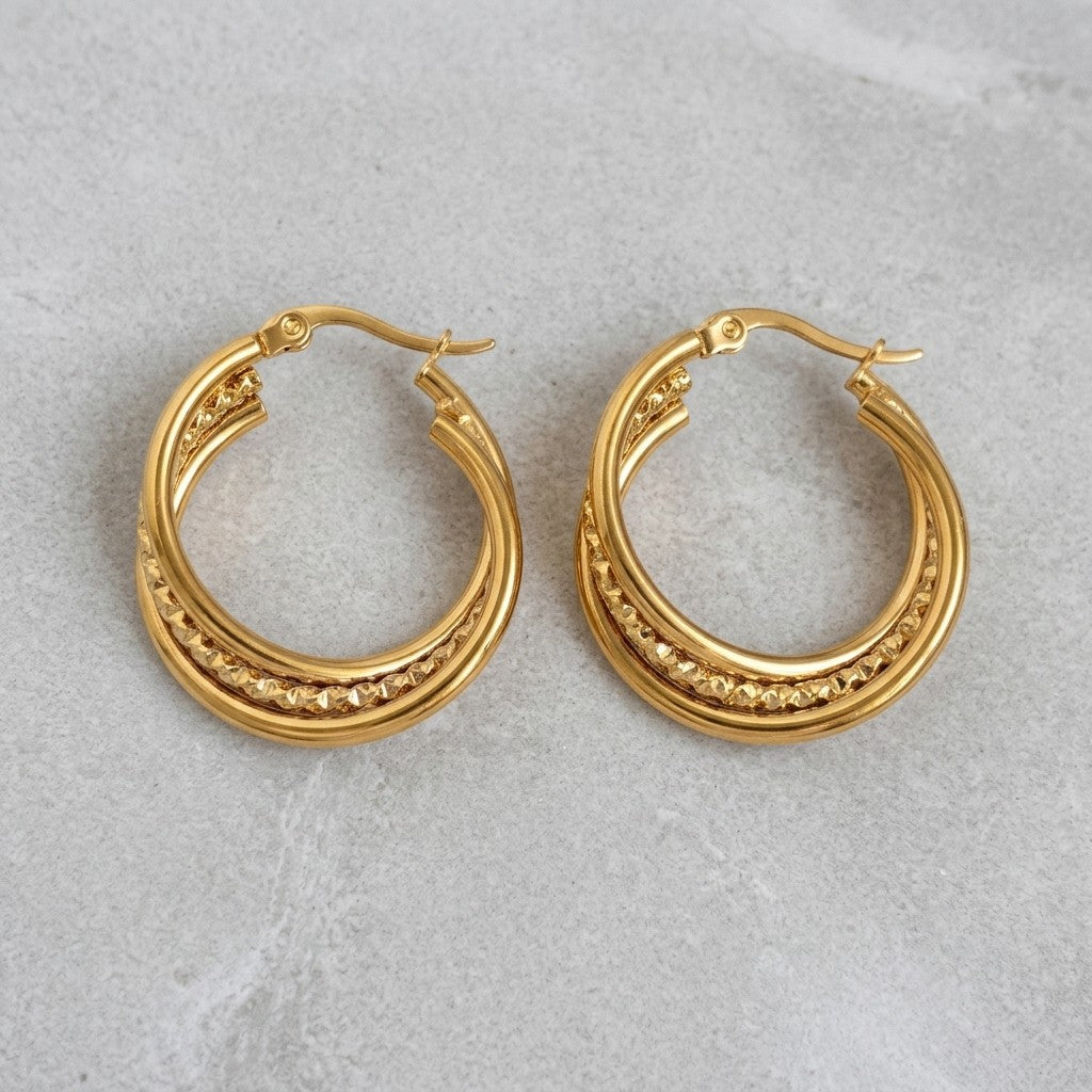 Aramat Jewels triple hoop earrings in gold-tone stainless steel with a twisted design and textured detail, 25mm diameter.