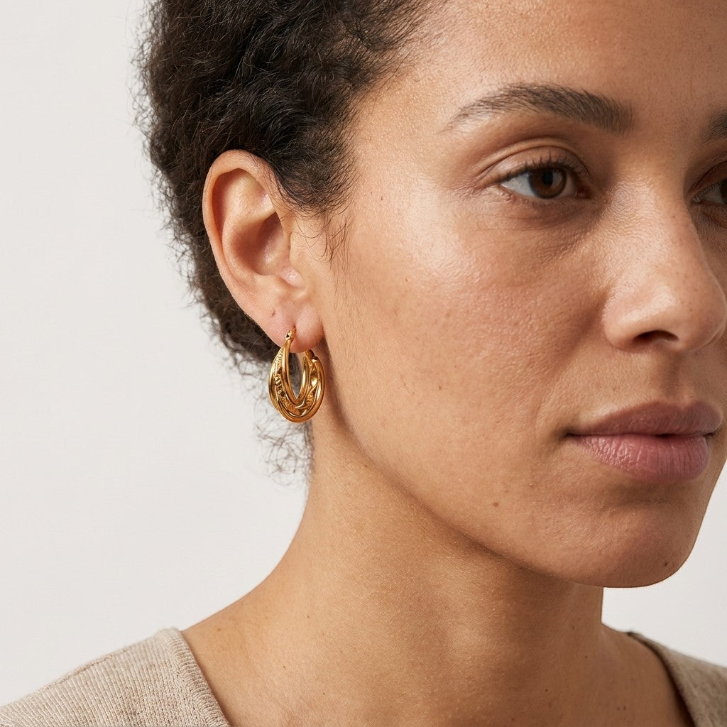 Aramat Jewels gold-tone stainless steel 20mm hoop earrings with a triple ring design, one twisted, worn by a model.