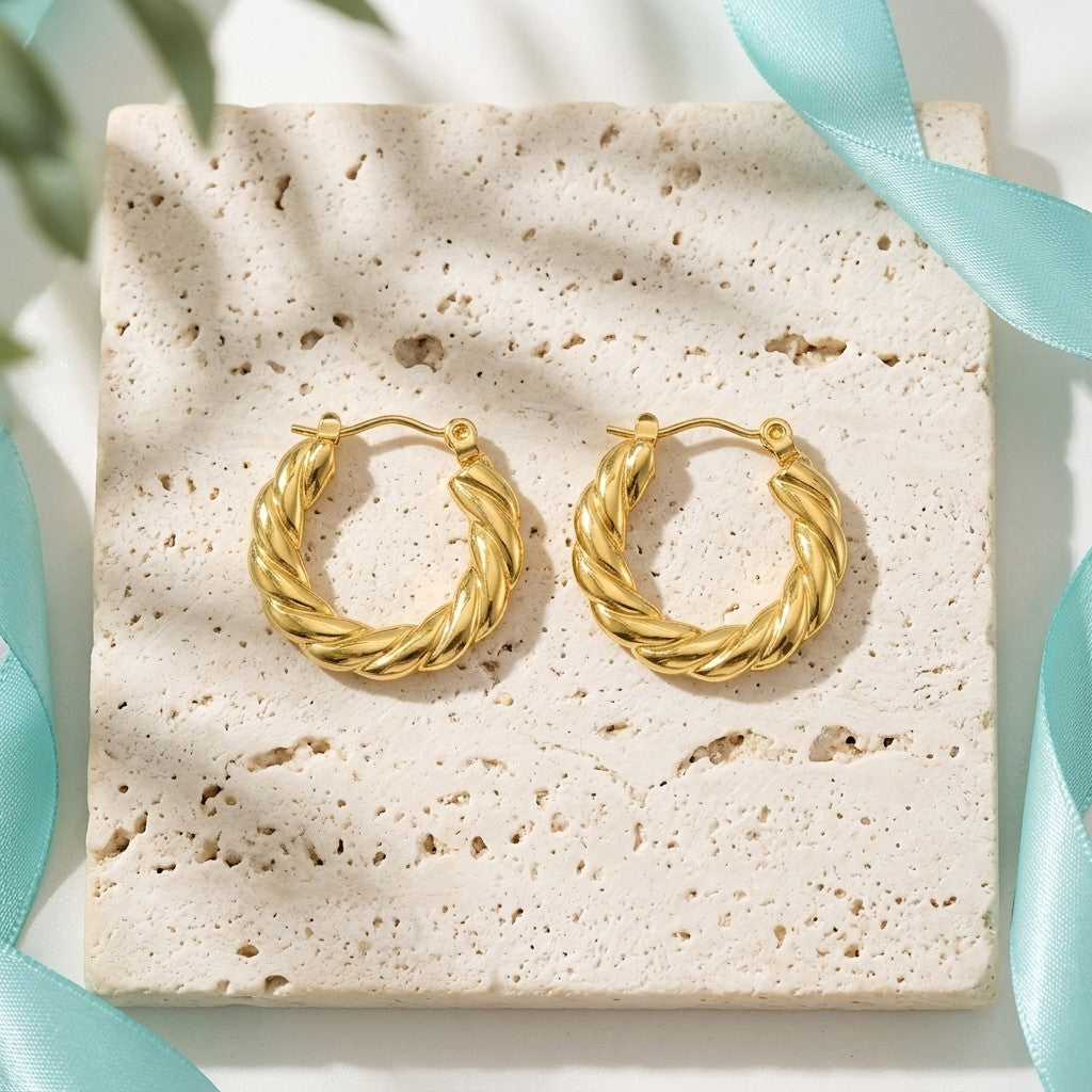 Aramat Jewels gold-tone stainless steel twisted hoop earrings, 23mm diameter, with diagonal stripe texture.