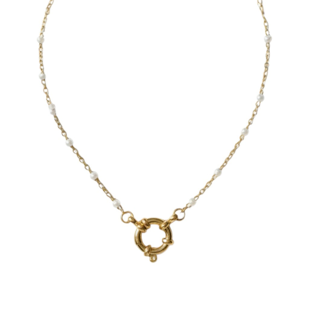 Aramat Jewels gold-tone stainless steel necklace with white enamel beads and a circular clasp, displayed on a branch.