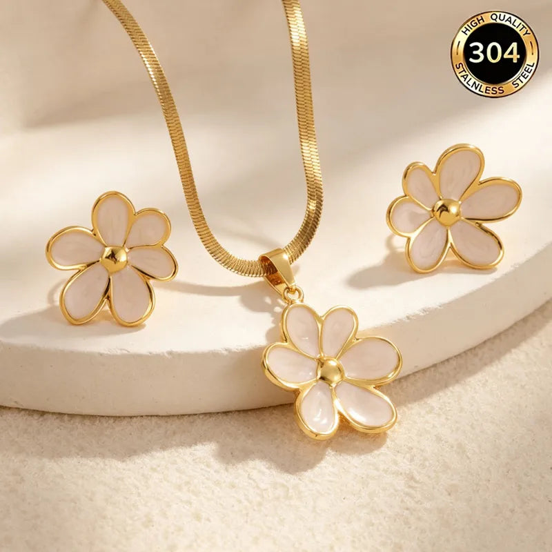 Aramat Jewels goudkleurige RVS sieradenset met witte emaille bloemhanger en bijpassende oorstekers op een witte ondergrond