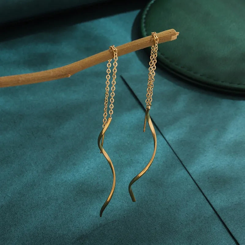 Aramat Jewels goudkleurige doortrek oorbellen van RVS met een elegant gedraaide staaf aan een fijn kettinkje.