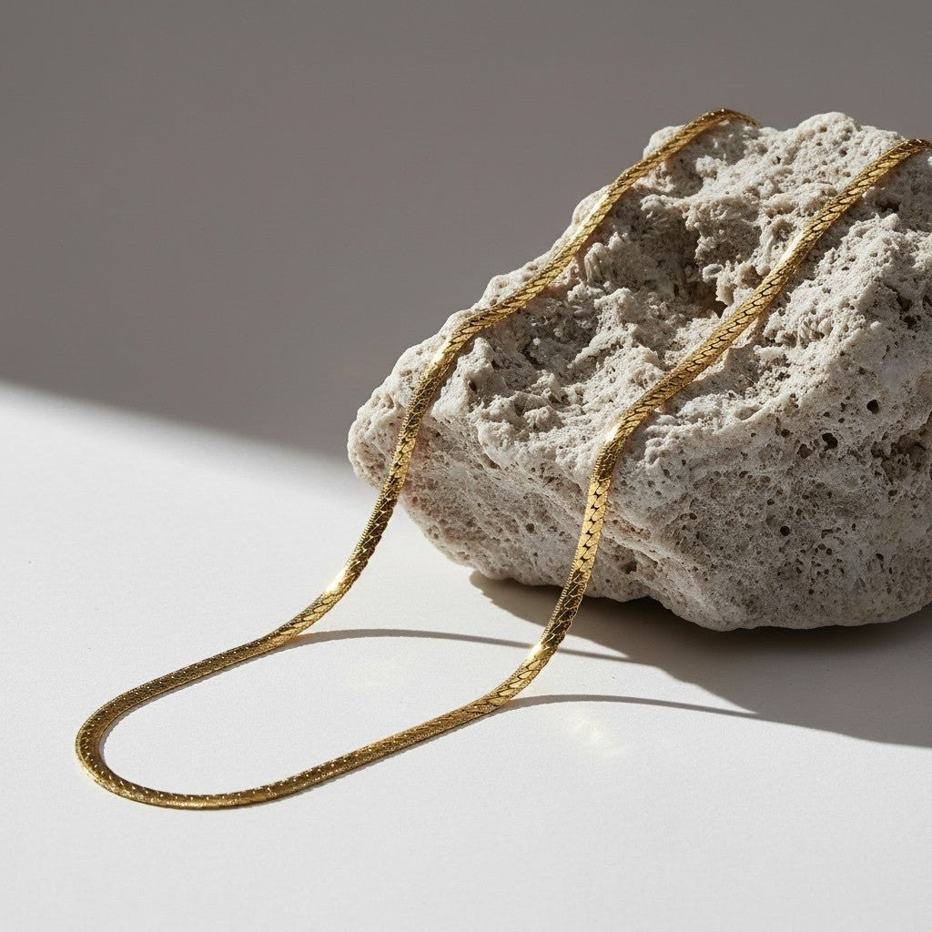 Aramat Jewels goudkleurige stalen gourmet ketting van 6mm breed met bewerkte rand, gepresenteerd op een ruwe steen.