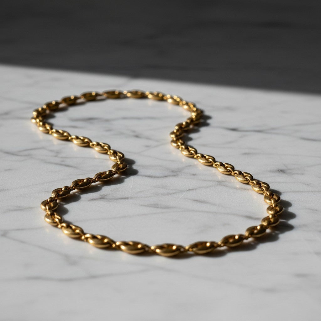 Aramat Jewels goudkleurige stalen koffieboon ketting van 4,5mm breed, een robuuste unisex schakelketting op marmer.