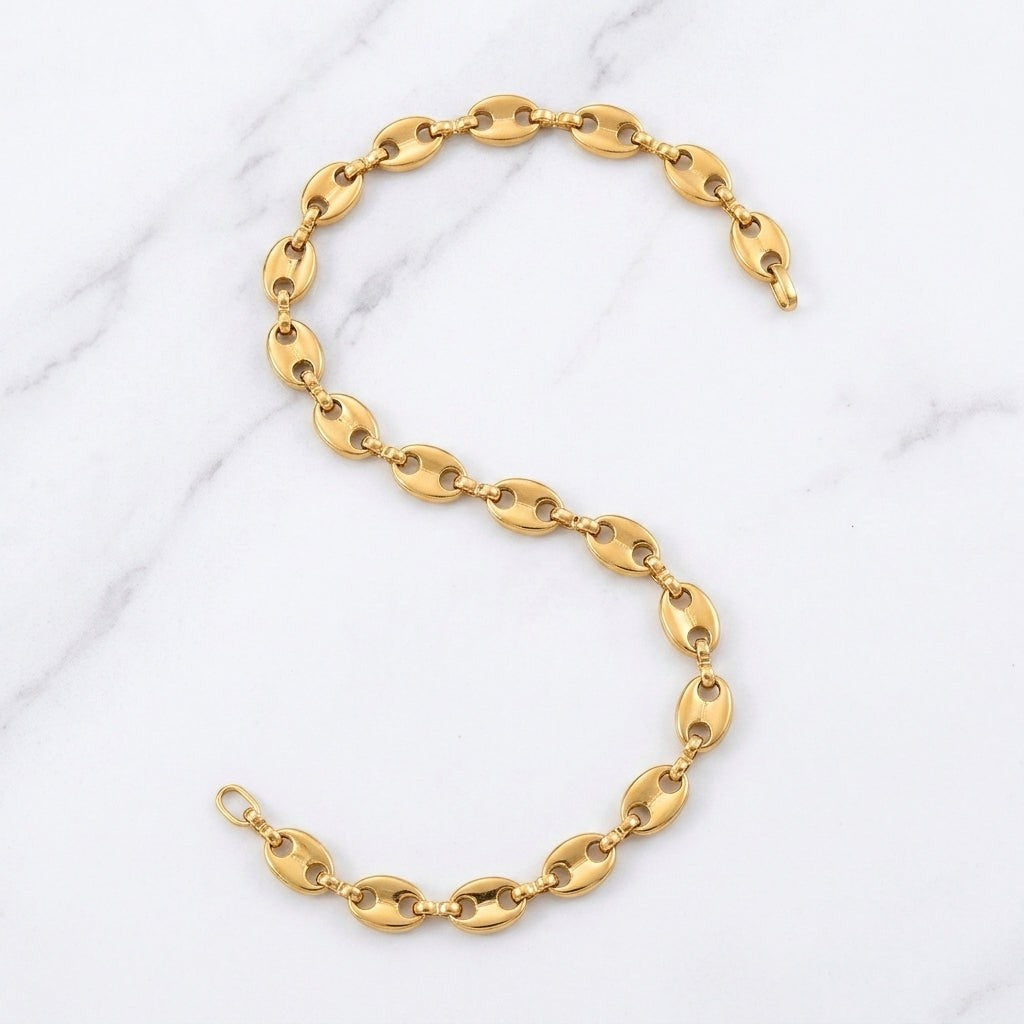 Aramat Jewels goudkleurige stalen koffieboon ketting van 60 cm met 5,2 mm schakels op een marmeren achtergrond.