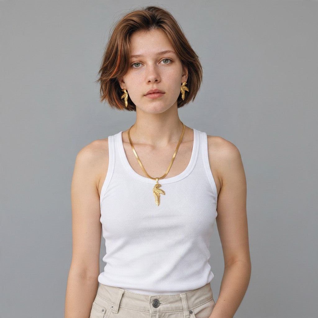 Aramat Jewels goudkleurige RVS sieradenset met half blad hanger en bijpassende oorbellen gedragen door een model.