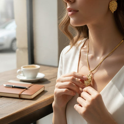 Aramat Jewels goudkleurige RVS sieradenset met blaadjeshanger aan een slangenketting en bijpassende blad-oorbellen.