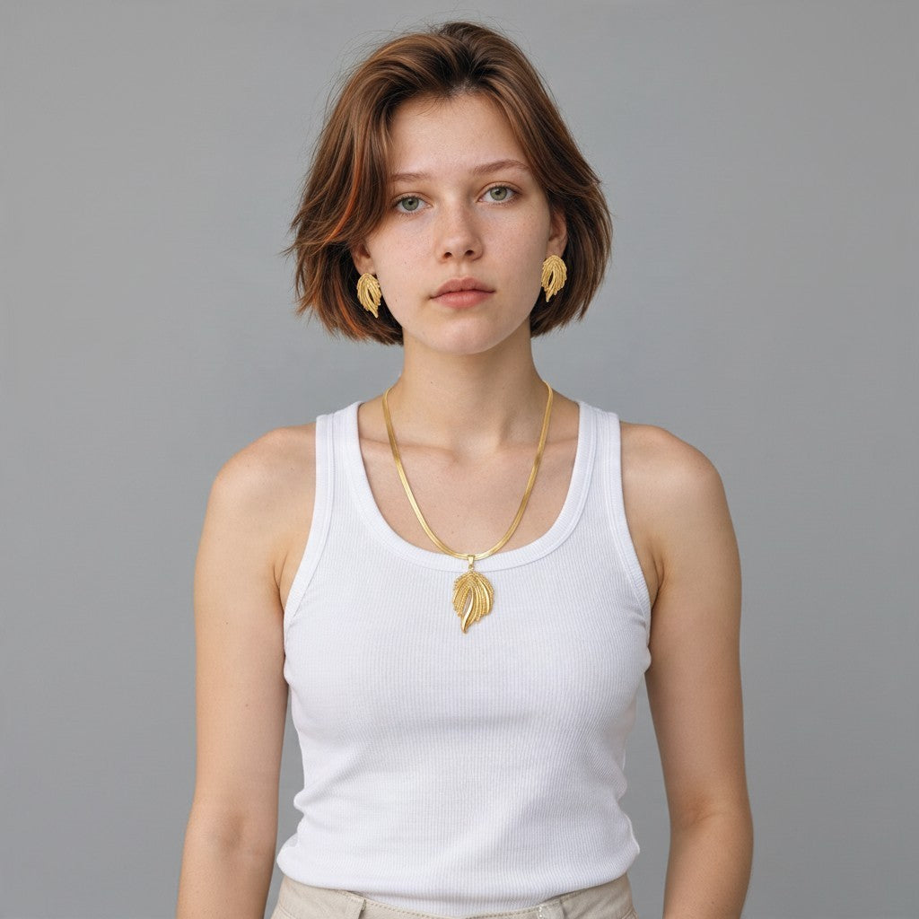 Model draagt Aramat Jewels goudkleurige RVS statement sieradenset met slangenketting en bijpassende fantasie oorbellen