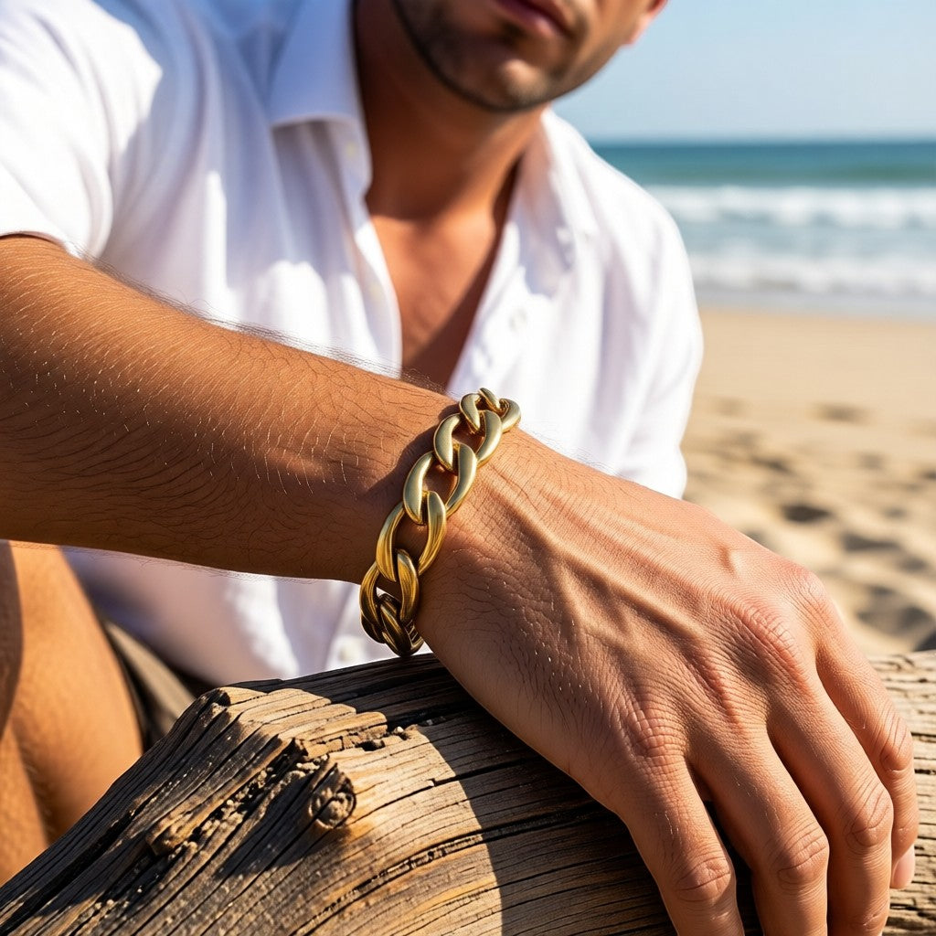 Aramat Jewels goudkleurige stalen gourmetarmband van 12 mm breed gedragen door een man op het strand.