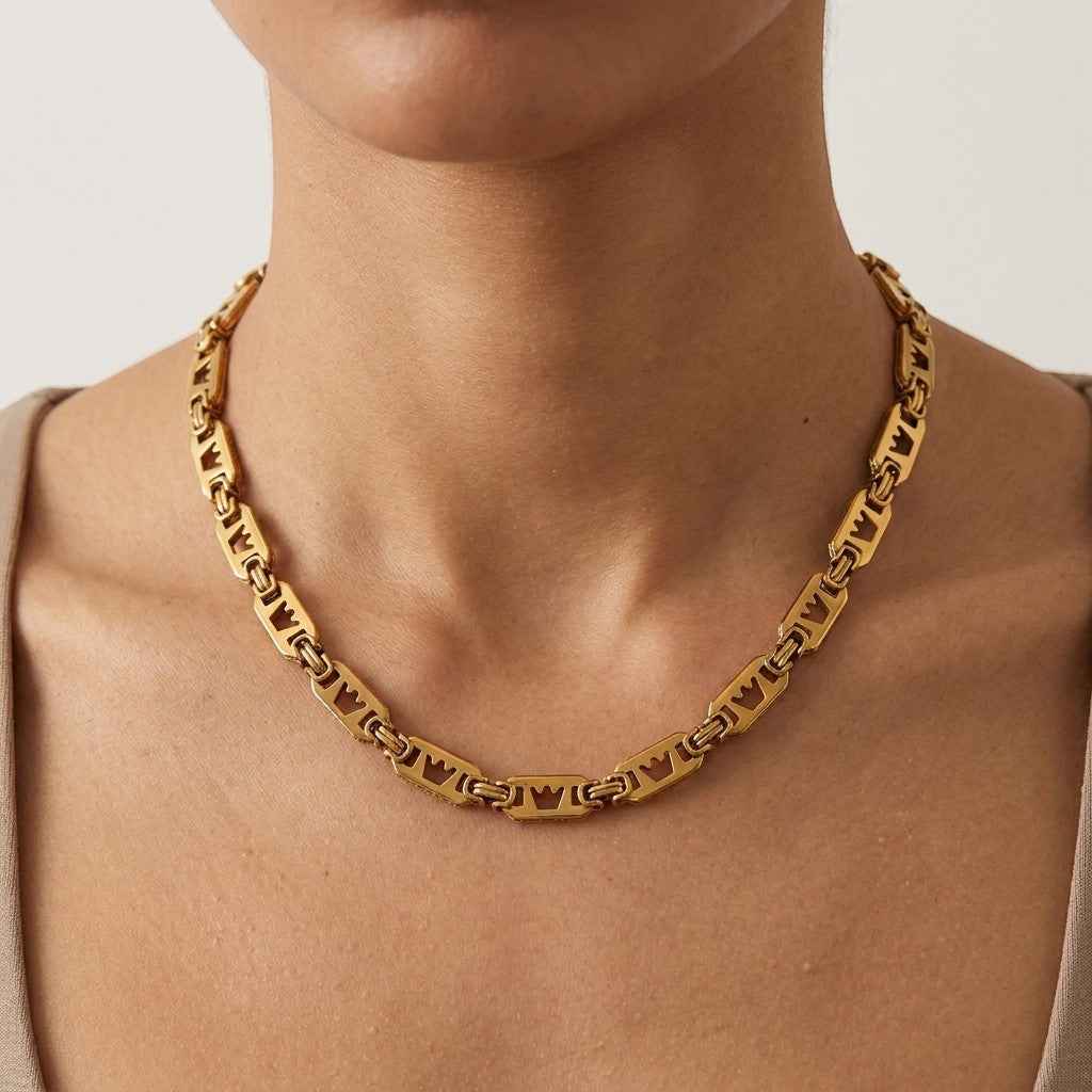 Brede Aramat Jewels koningsketting van goudkleurig roestvrij staal met unieke kroonmotief schakels om een hals.
