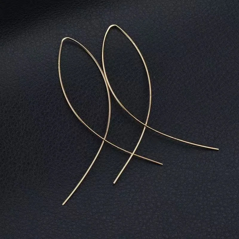 Aramat Jewels goudkleurige doortrek oorbellen in een minimalistische geometrische visvorm op een zwarte achtergrond.