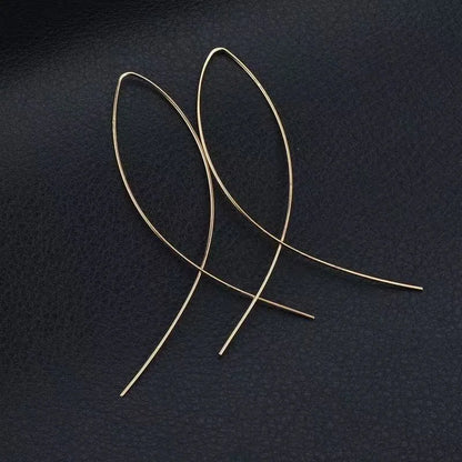 Aramat Jewels goudkleurige doortrek oorbellen in een minimalistische geometrische visvorm op een zwarte achtergrond.