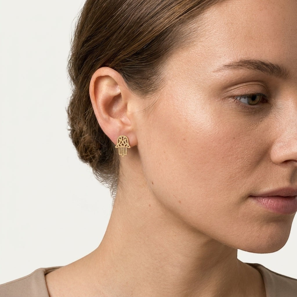 Aramat Jewels goudkleurige Hamsa oorstekers van RVS met een matte, gezandstraalde afwerking gedragen door een model.