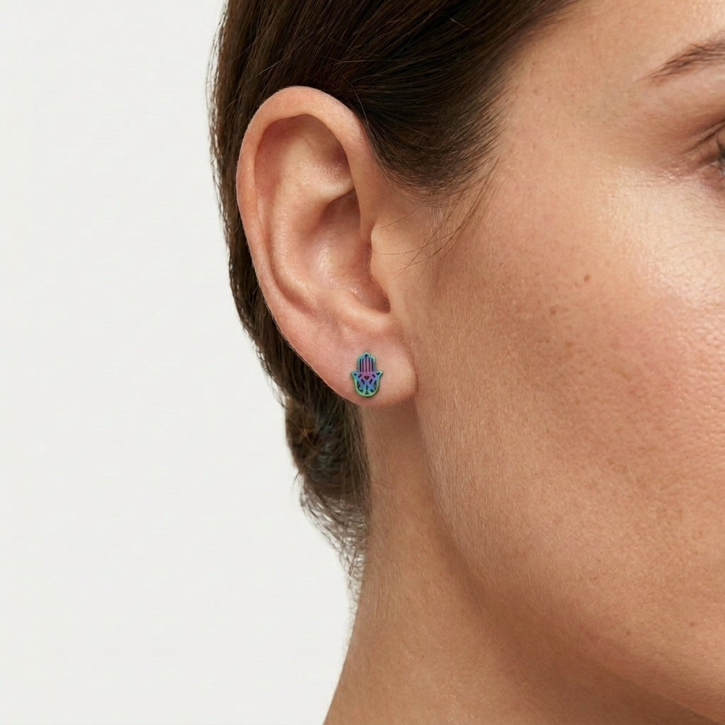 Aramat Jewels Hamsa handje van Fatima oorknopjes van RVS met een unieke regenboogkleurige afwerking in een oor.