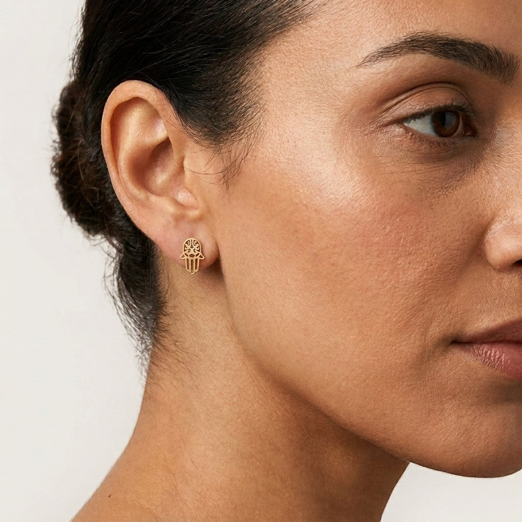 Aramat Jewels goudkleurige Hamsa hand oorknopjes van RVS gedragen door een vrouw voor een elegante look.