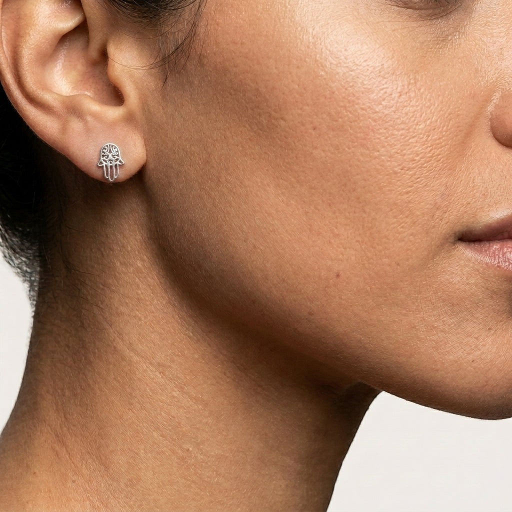 Aramat Jewels zilverkleurige Hamsa hand oorknopjes van RVS gedragen in een oor voor een minimalistische look.
