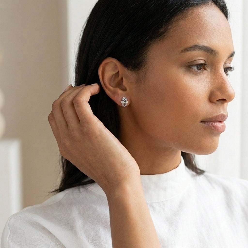 Model draagt zilverkleurige Aramat Jewels Hamsa oorstekers van RVS in de vorm van een Handje van Fatima.
