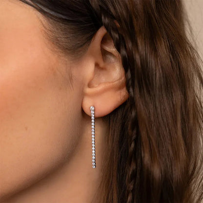Aramat Jewels lange goudkleurige RVS oorhangers met een rij transparante kristallen gedragen in een oor