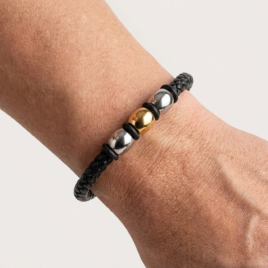 Aramat Jewels gevlochten zwarte leren herenarmband met zilver- en goudkleurige stalen kralen om een pols.