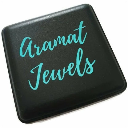 Aramat Jewels logo in turquoise script op een zwarte vierkante achtergrond.