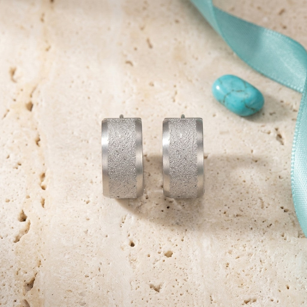 Aramat Jewels matte silver stainless steel hoop earrings with a sandblasted stripe detail. Modern contrast design.