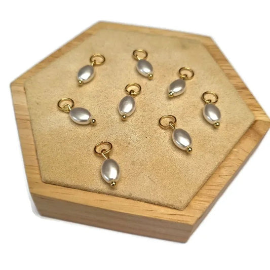 Aramat Jewels oval synthetic pearl charms with gold-tone metal loops displayed on a beige hexagonal wooden stand.