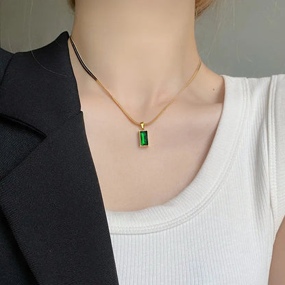 Aramat Jewels goudkleurige platte slangenketting met een rechthoekige groene zirkonia hanger om een hals gedragen.