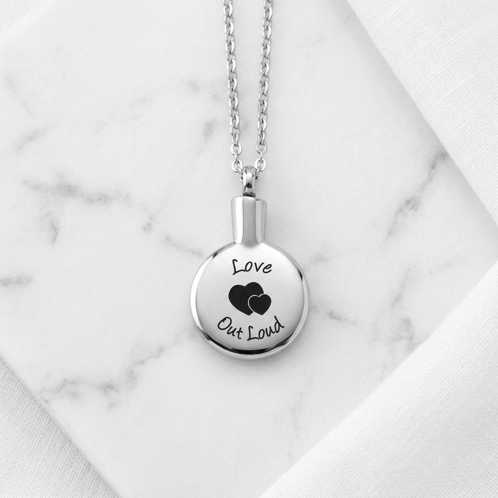 Aramat Jewels zilverkleurige ronde ashanger met gravure 'love out loud' en twee hartjes, gemaakt van roestvrij staal.