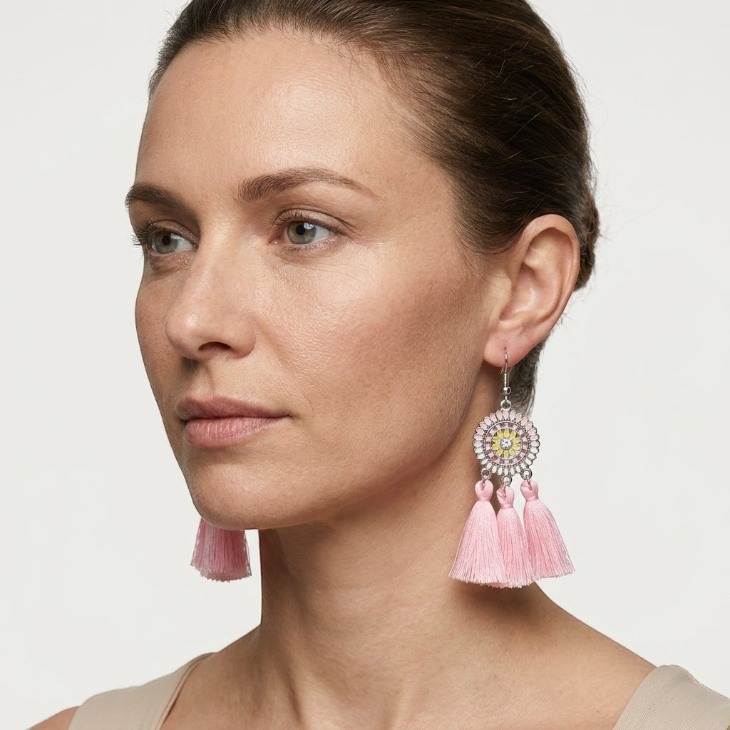 Model draagt Aramat Jewels boho oorhangers met licht roze kwastjes, emaille details en glanzend roestvrij staal.
