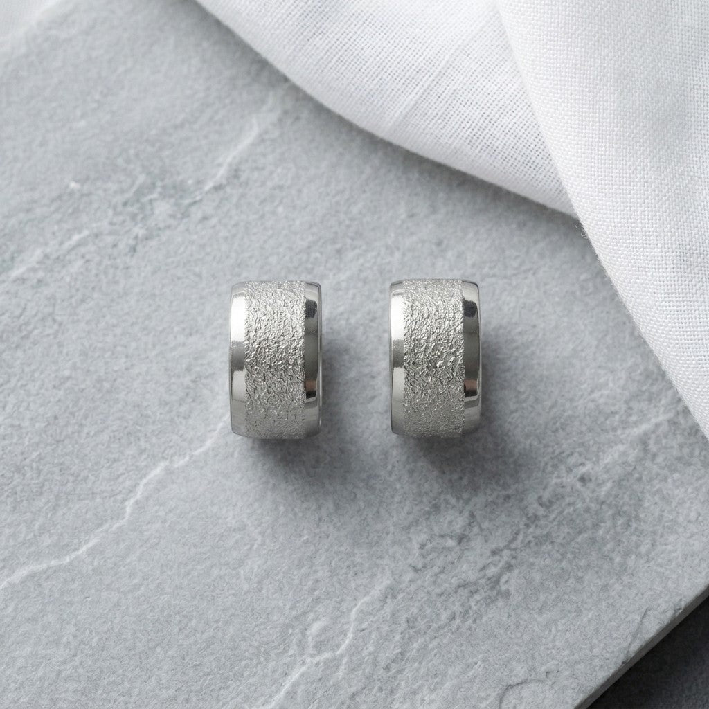 Aramat Jewels sandblasted silver-tone stainless steel huggie hoop earrings, 13mm wide with a textured finish.