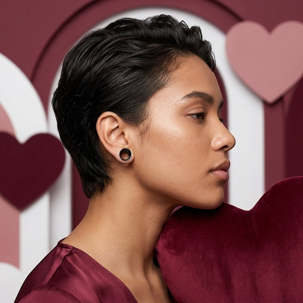 Aramat Jewels flexibele zwarte siliconen oortunnels van 8mm gedragen door een vrouw met kort haar voor een hartjesachtergrond