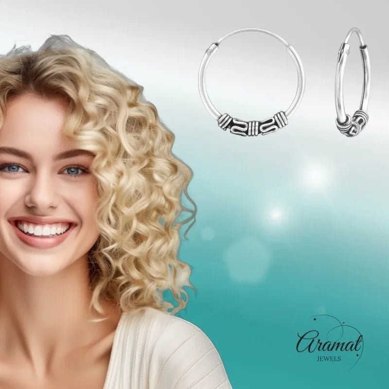 Aramat Jewels unisex 16mm silver Bali hoop earrings with intricate tribal detailing. Model with blonde curly hair smiles.