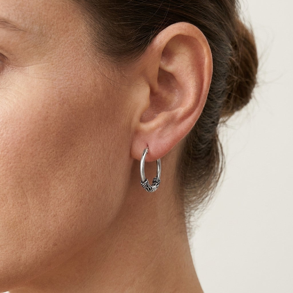 Aramat Jewels thin 16mm silver Bali hoop earrings with intricate detailing, worn by a model.
