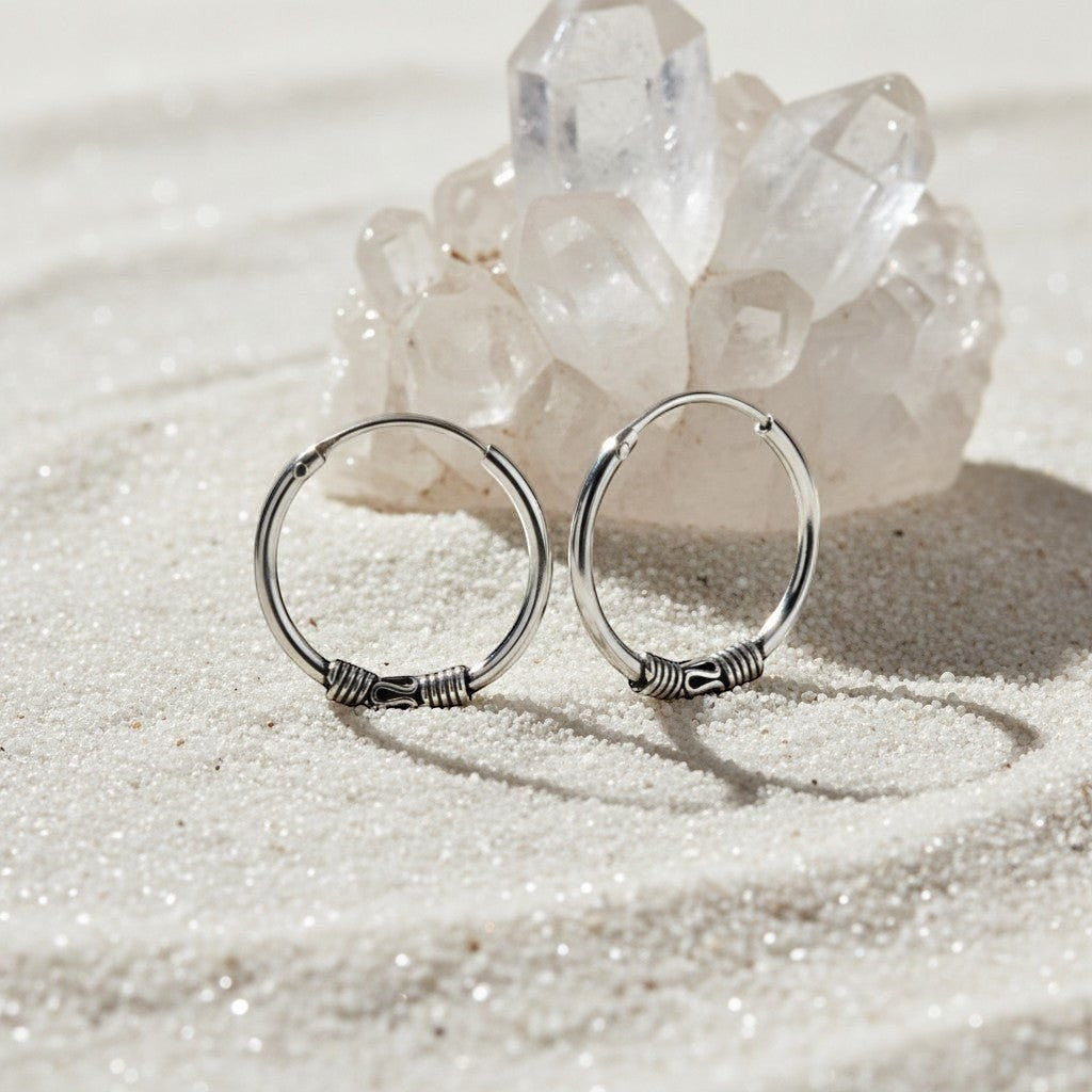 Aramat Jewels unisex 16mm silver Bali hoop earrings with intricate wire detailing, set on a sandy surface with a crystal formation.