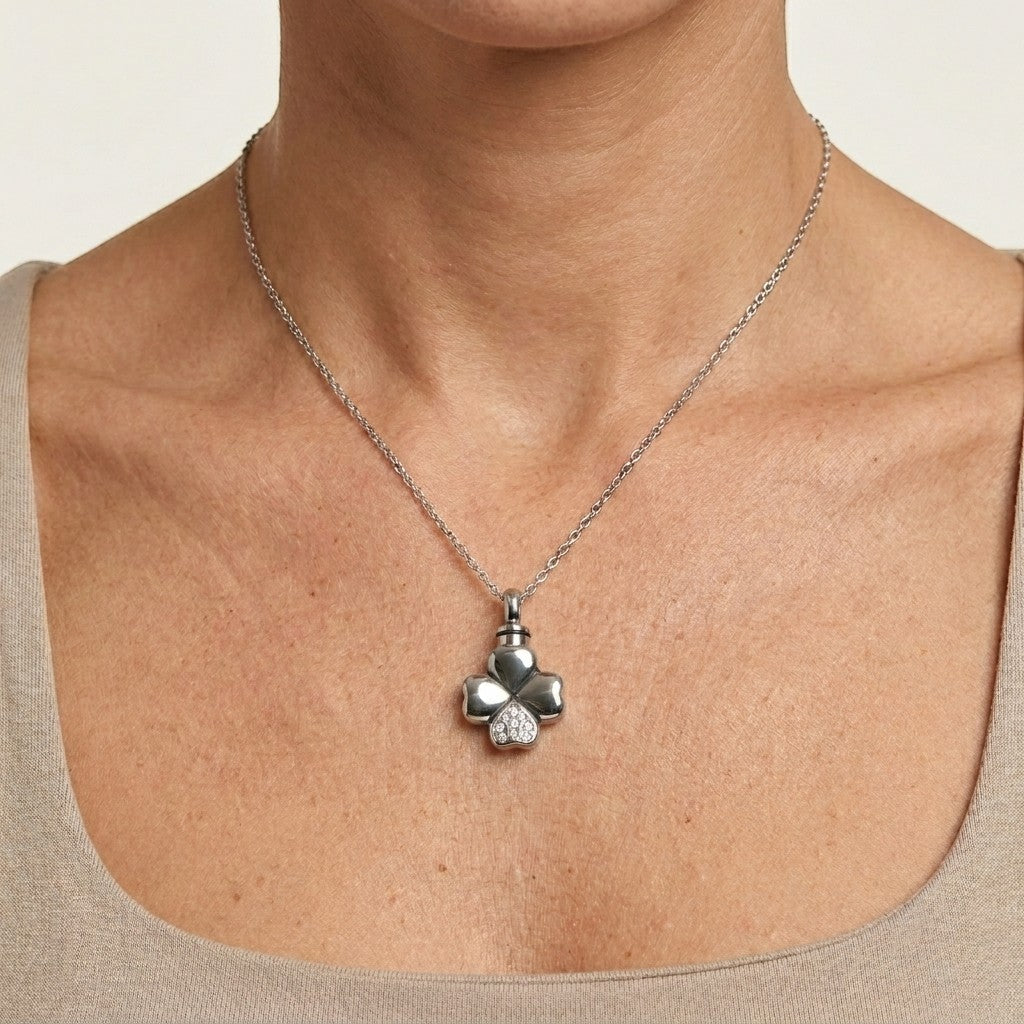 Aramat Jewels silver-tone stainless steel four-leaf clover cremation pendant with clear cubic zirconia accents, worn on a delicate chain around a woman's neck.