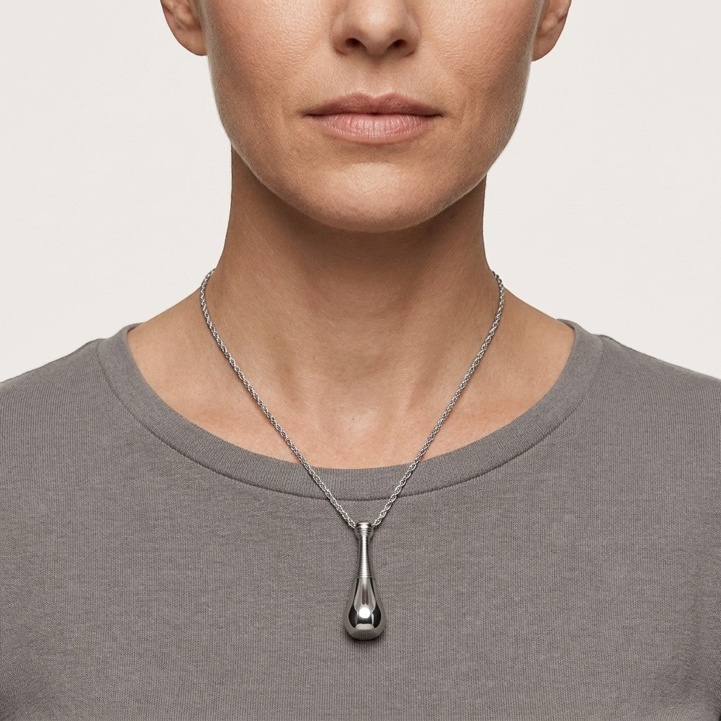 Aramat Jewels silver-colored 316L steel cone urn pendant on a rope chain necklace worn by a woman.