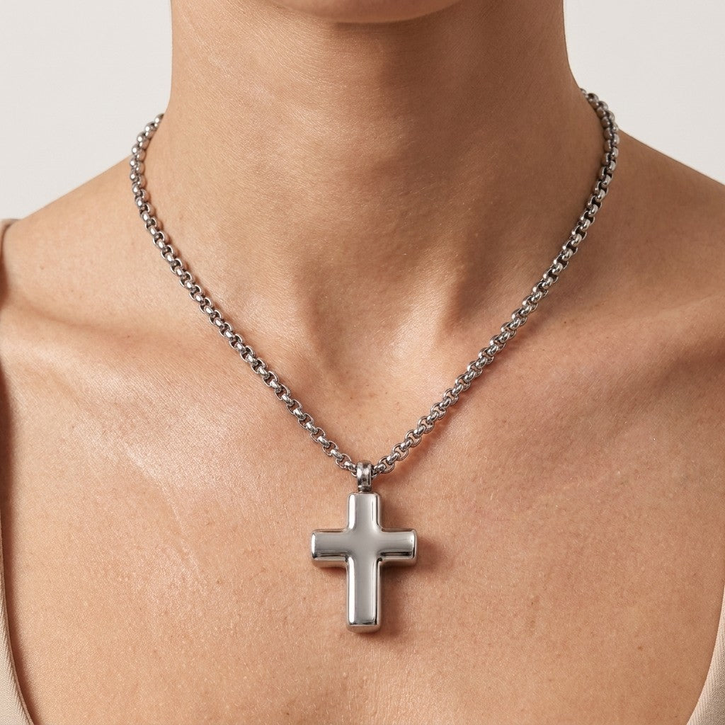 Aramat Jewels silver-colored 316L steel cross pendant ashanger, 2x1.5cm, on a matching chain worn by a person.