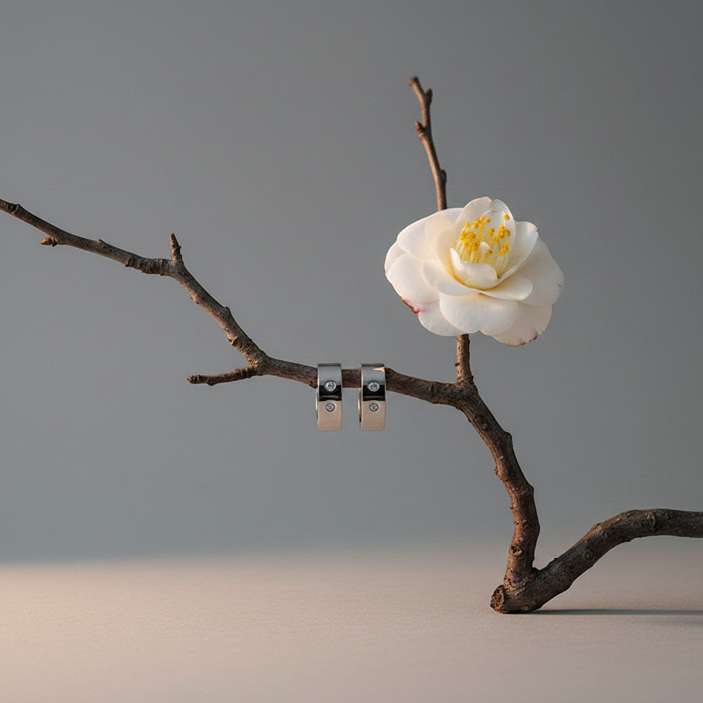 Aramat Jewels wide silver-tone huggie hoop earrings with clear crystals, 20mm, displayed on a branch with a white flower.