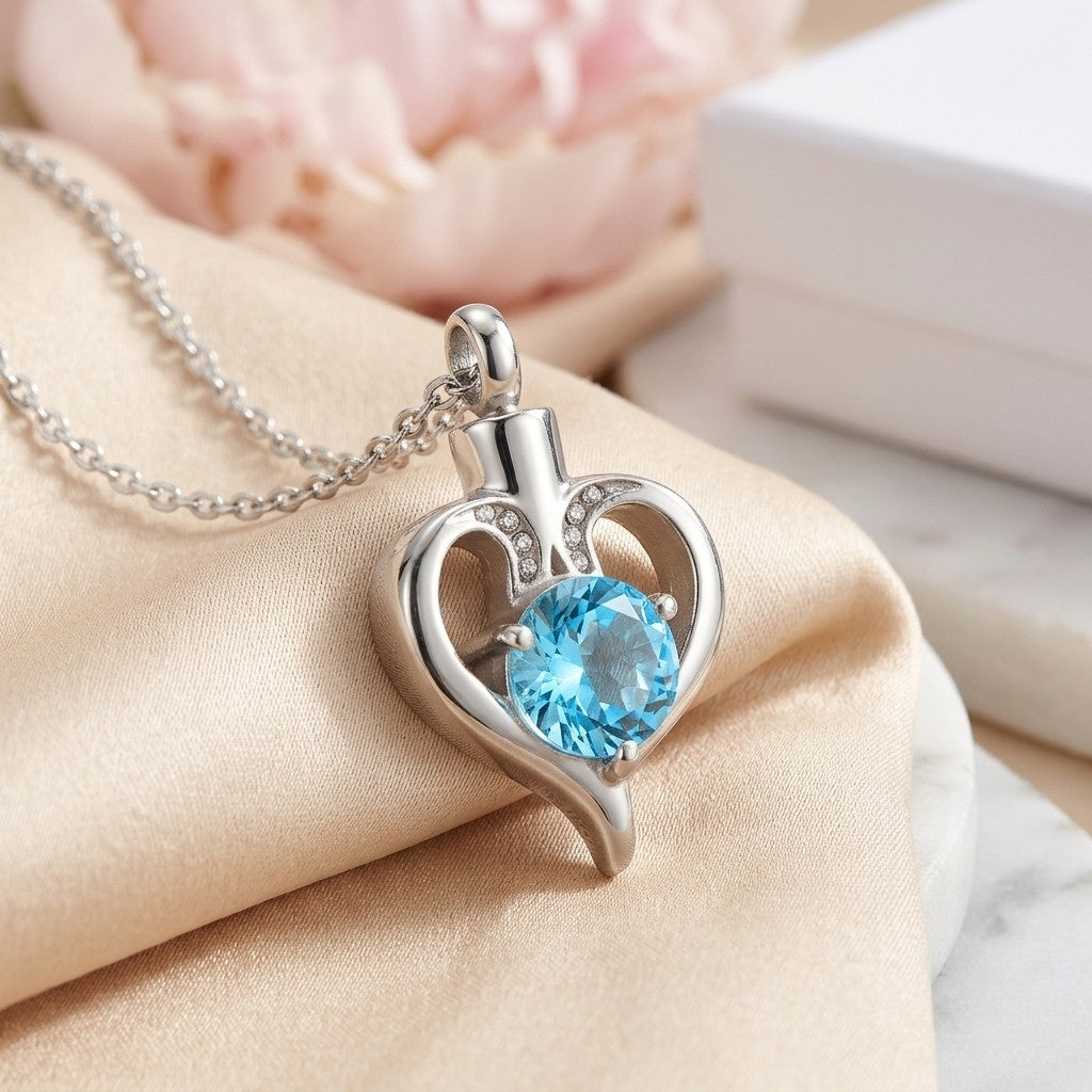 Aramat Jewels silver-tone stainless steel heart-shaped cremation urn pendant with a large blue cubic zirconia and small clear stones.