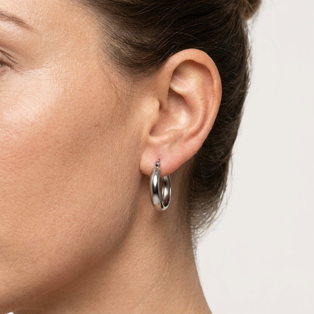 Aramat Jewels silver-tone stainless steel hoop earrings, 20mm diameter, smooth polished finish, worn by a model.