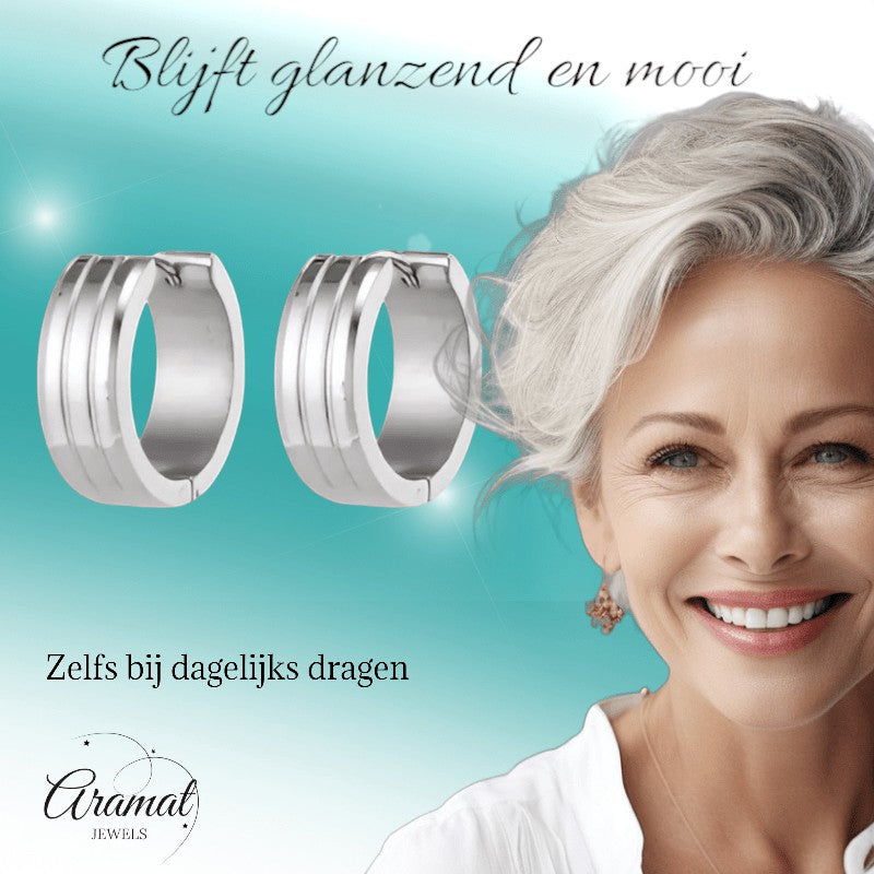 Aramat Jewels silver-tone stainless steel hoop earrings with three raised stripes, 20mm diameter, 7mm width. Model wears them with a white top.