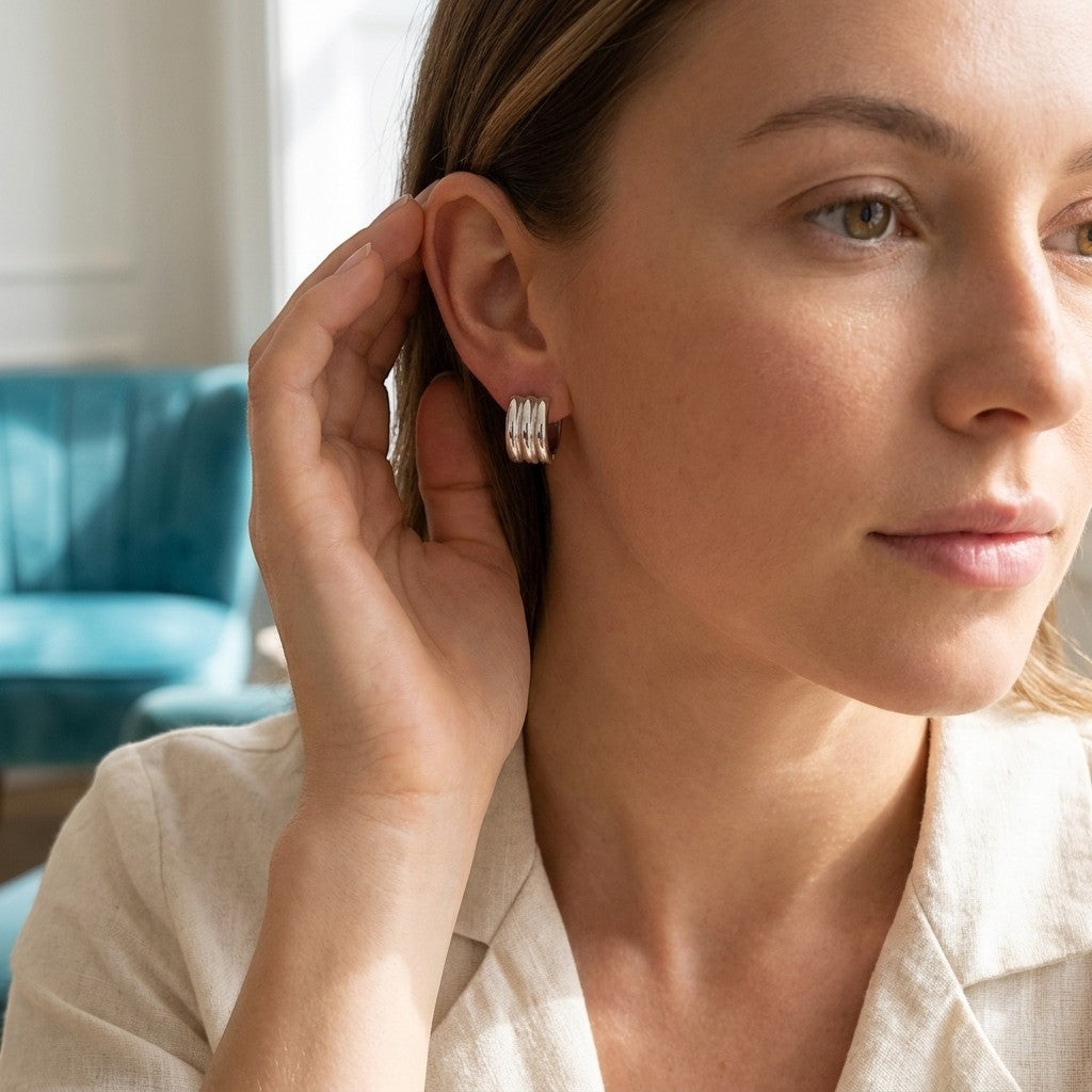 Aramat Jewels wide silver-tone stainless steel hoop earrings with ribbed detail, worn by a woman.