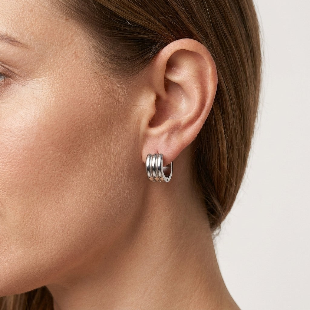 Aramat Jewels wide silver-tone stainless steel hoop earrings with three parallel ridges, worn by a woman.