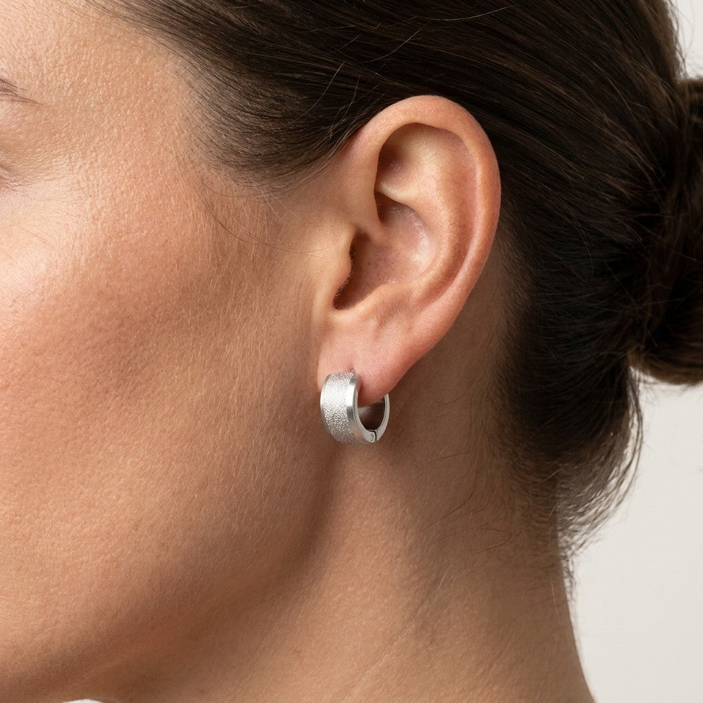 Aramat Jewels matte silver-colored stainless steel hoop earrings with a sandblasted stripe detail. The earrings are 13mm in diameter and 7mm wide.