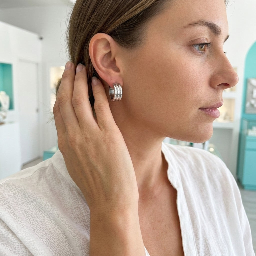Aramat Jewels wide silver-tone stainless steel hoop earrings with three stacked bands, worn by a woman.
