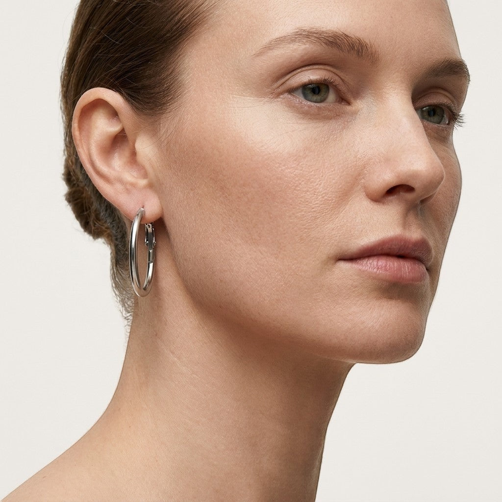 Aramat Jewels silver-tone stainless steel hoop earrings with a high-gloss finish, worn by a model.